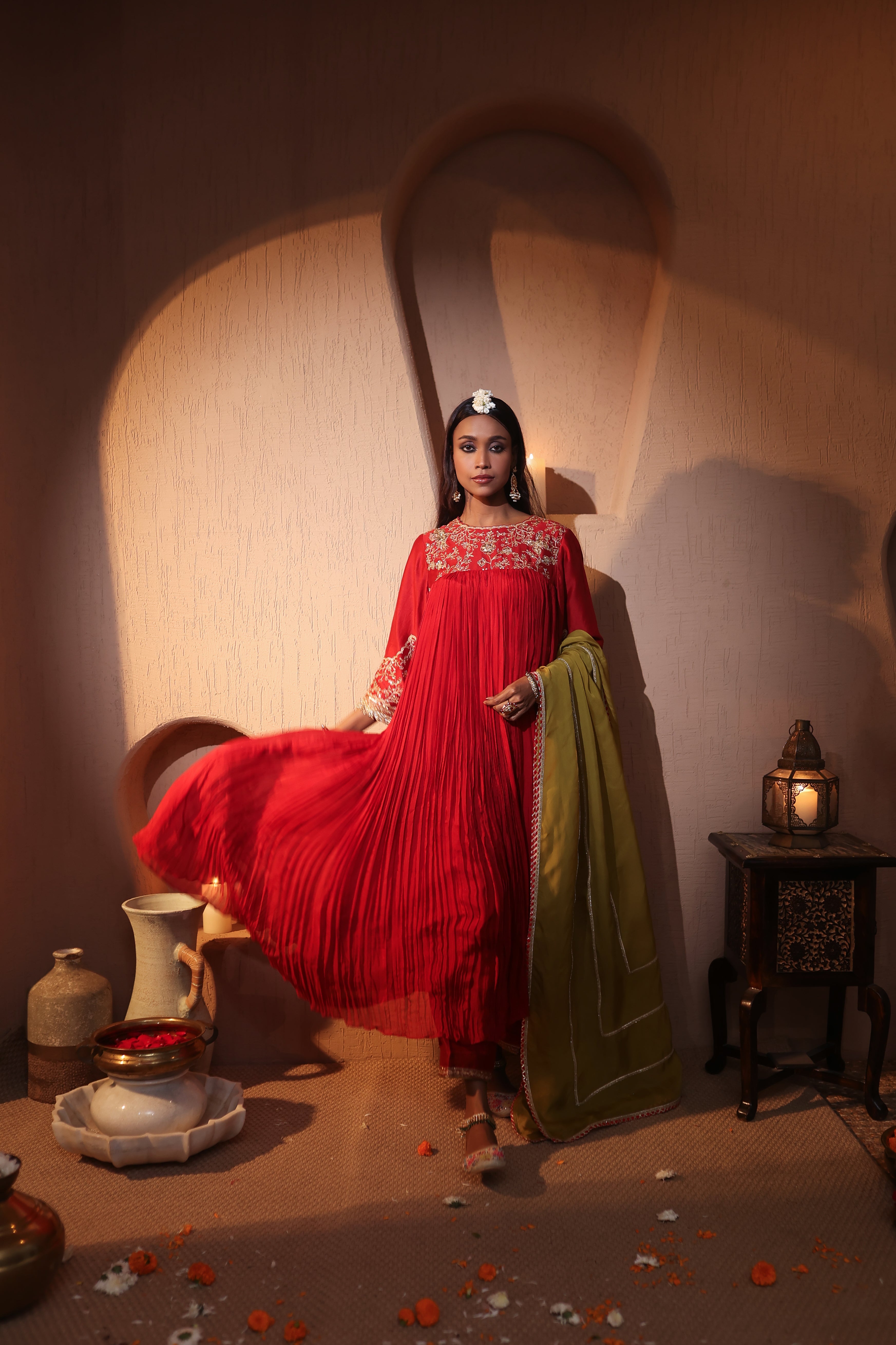 Woman in a red silk chanderi kurta set with zari hand embroidered traditional outfit standing in a warm-toned room with decorative elements.