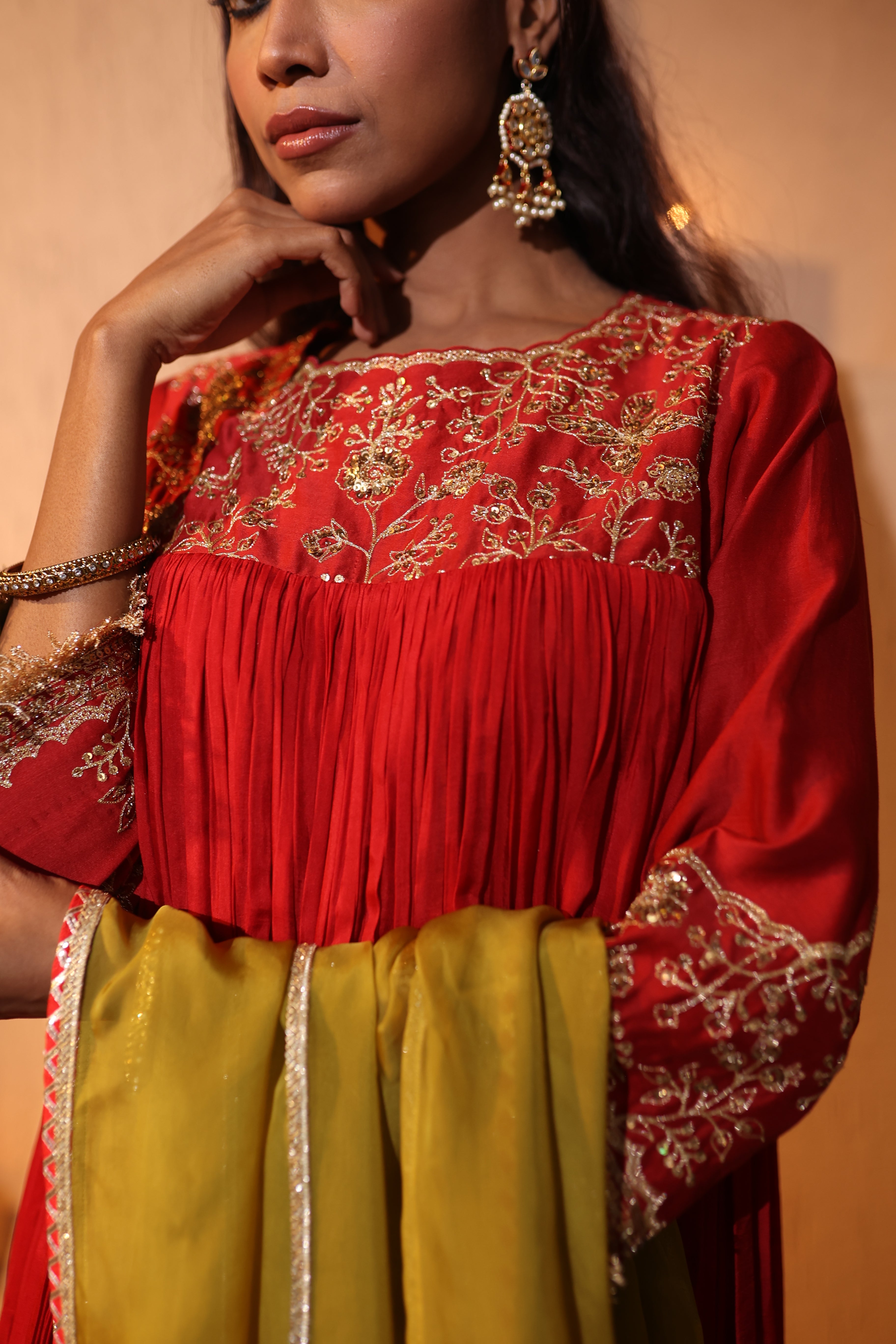 Woman wearing a silk chanderi red and gold zari hand embroidered top with a beige background
