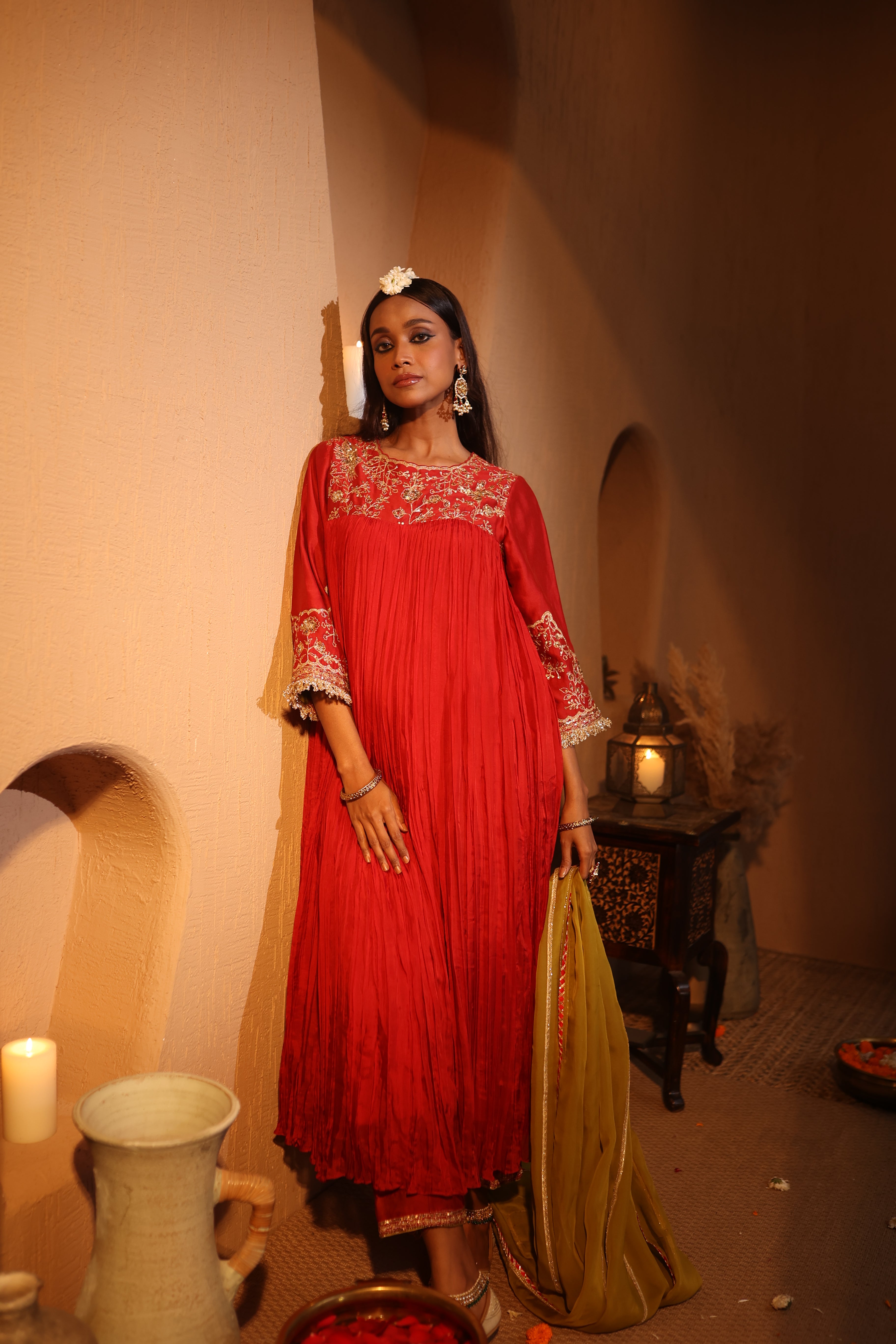 Woman in a red silk chanderi kurta set with zari hand embroidery standing in a warm-toned room with decorative elements.
