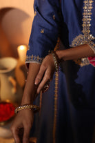 Woman wearing a blue traditional kurta set with gold embroidery, holding a hand with bangles.

