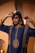 Woman wearing a blue embroidered silk chanderi kurta set with gold zari hand embroidery details, posing indoors.