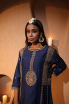 Woman wearing a blue gold zari hand embroidered kurta set in a warm-toned room. 