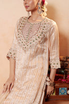 Woman wearing a traditional outfit with intricate patterns in a warm-toned setting.
