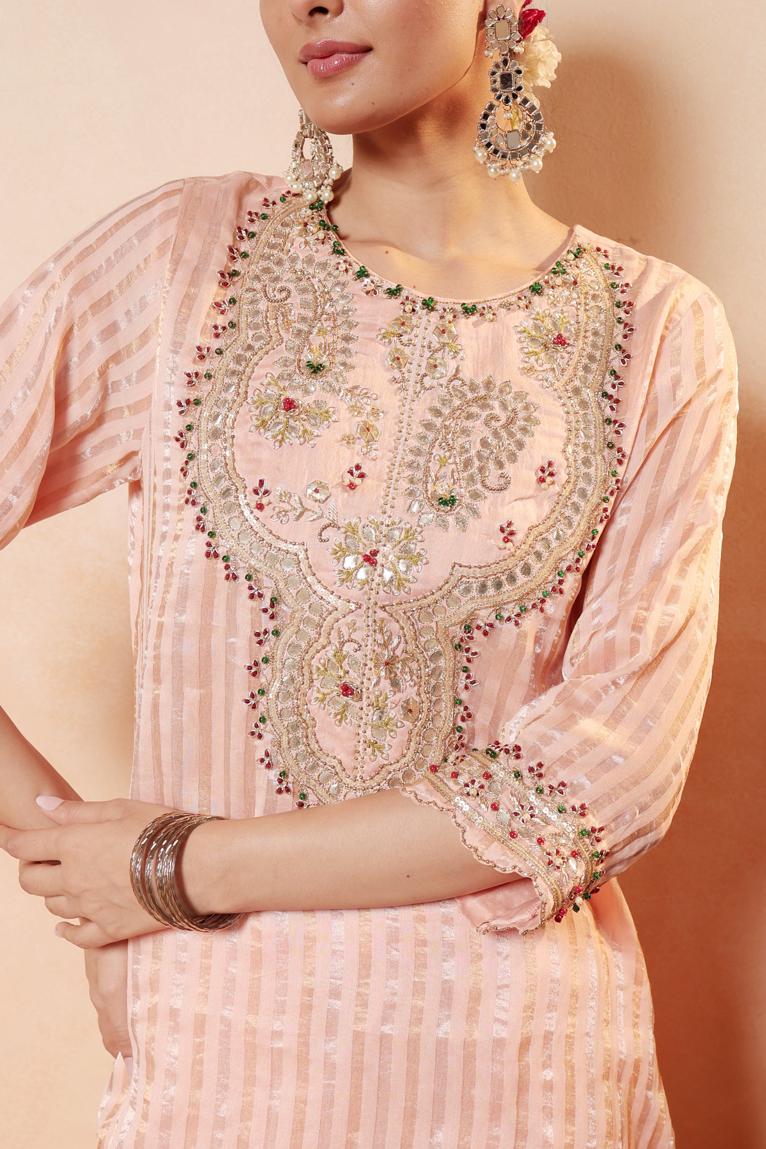Woman wearing a Peach embroidered with gota traditional outfit with jewelry on a beige background