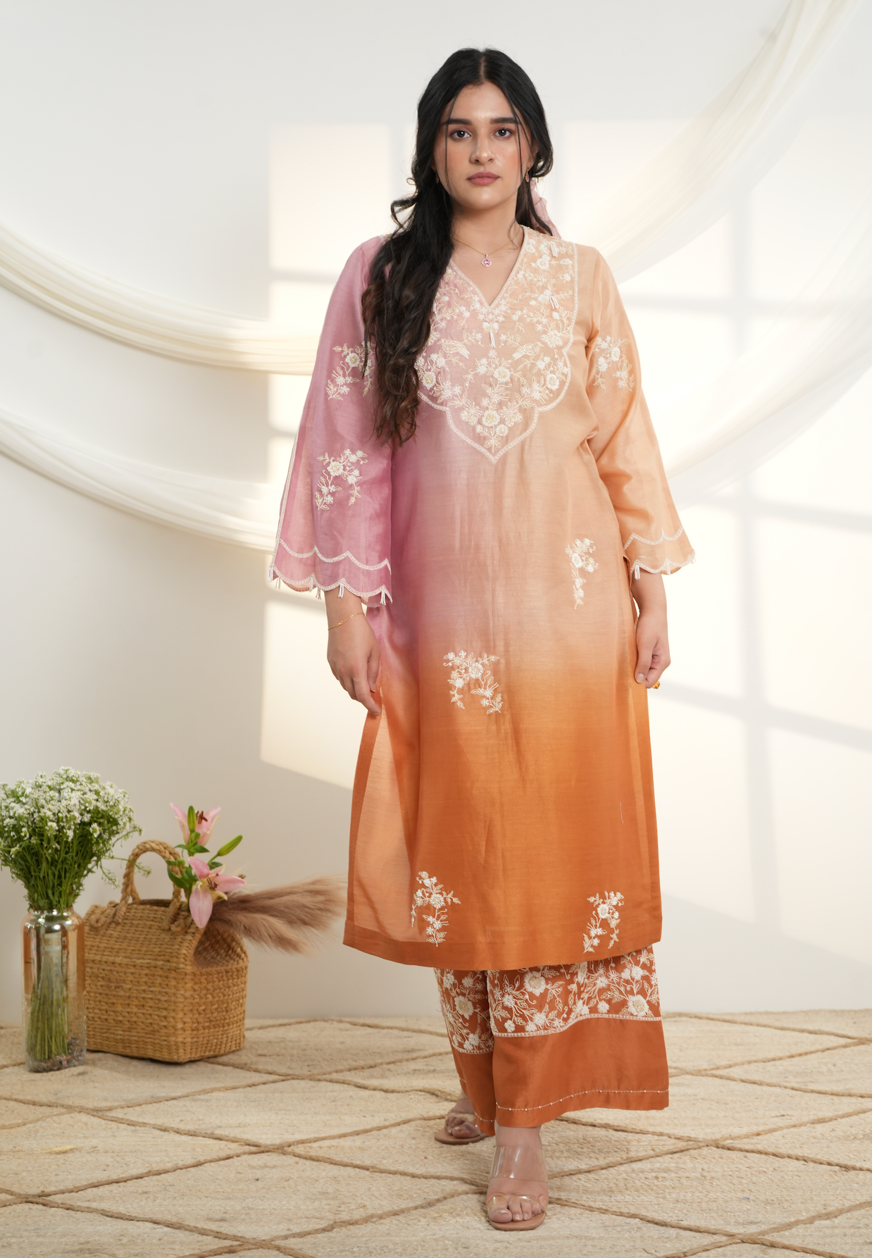 Model wearing a peach & pink ombre silk chanderi kurta set with off-white dori and bead embroidery, styled with floral embroidered wide-leg pants.