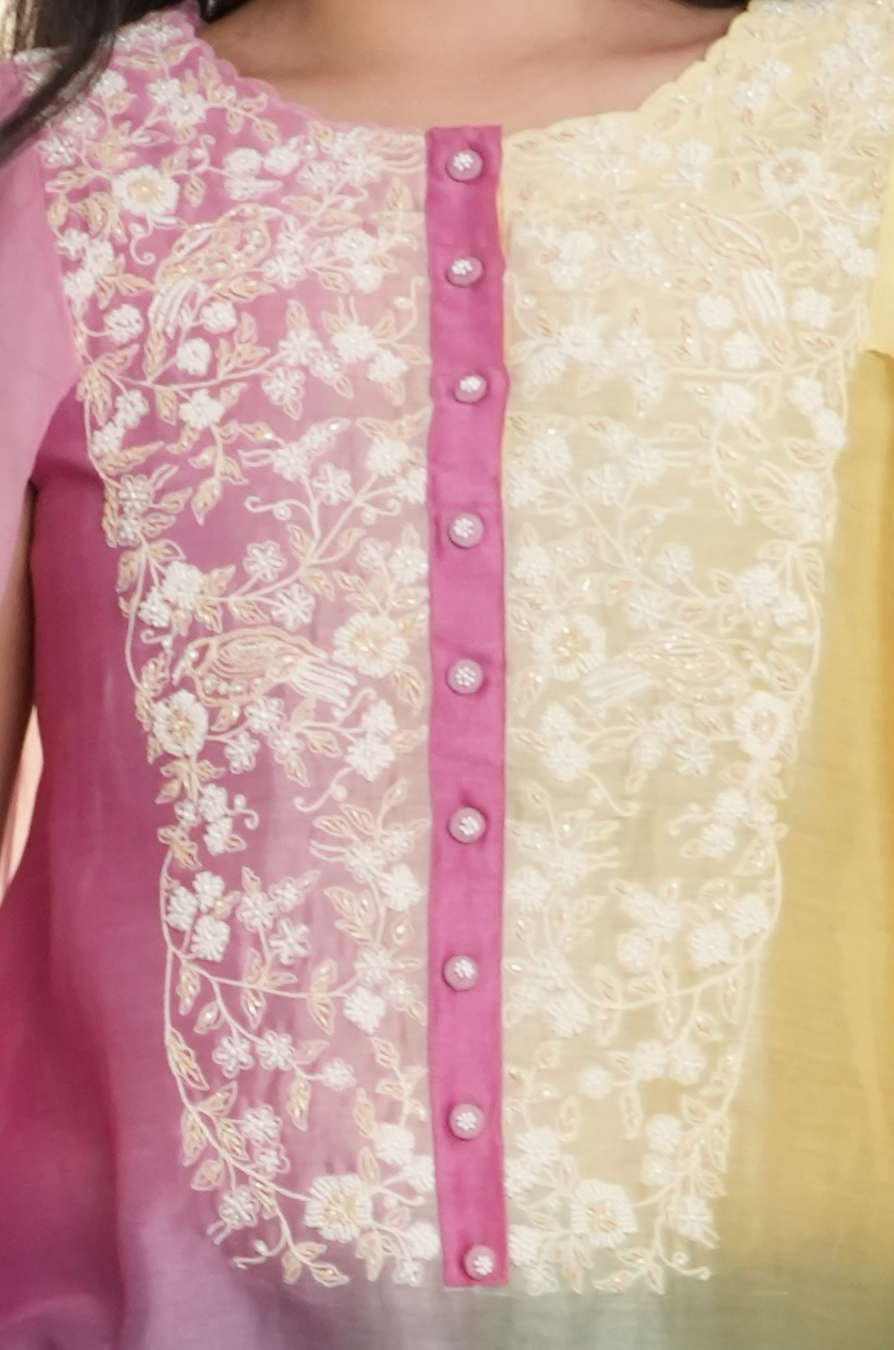 Close-up of a traditional outfit with pink and white floral embroidery on a light yellow background.
